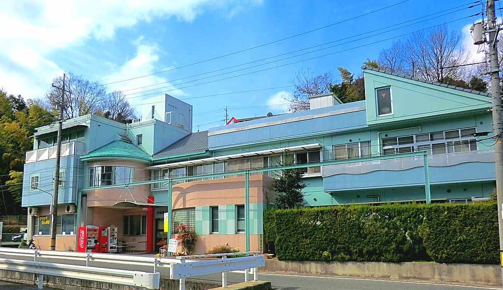 緑色の屋根と壁が特徴的な介護施設の建物外観。入口には赤い庇があり、周囲は緑に囲まれている。